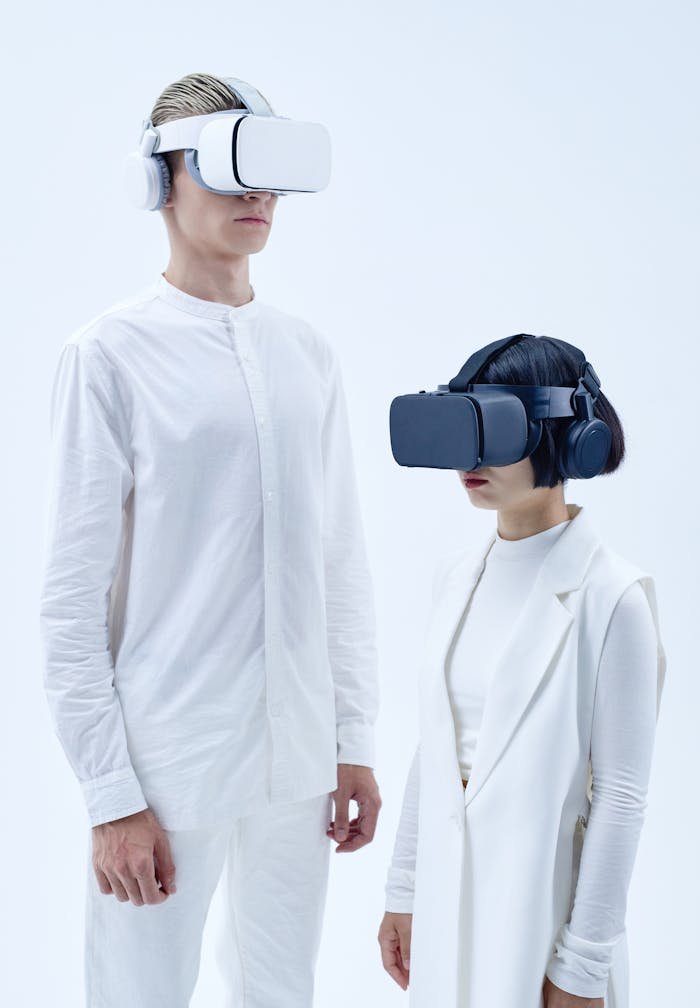 Man and woman in white clothes wearing VR headsets against plain background.